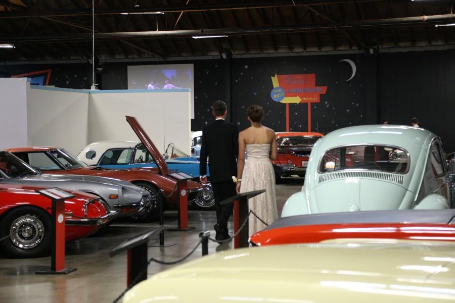 Students walk through the prom venue, looking at vintage cars. 