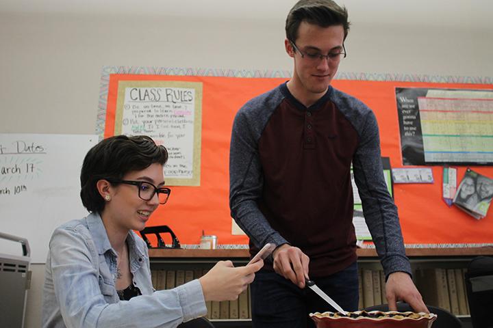 In Mrs. Abigail Pena’s room during lunch, Emma Gloudeman takes a photo while Ashton Davis cuts the blueberry cardamom pie he made in honor of Pi Day. Photo by Danica Tran.