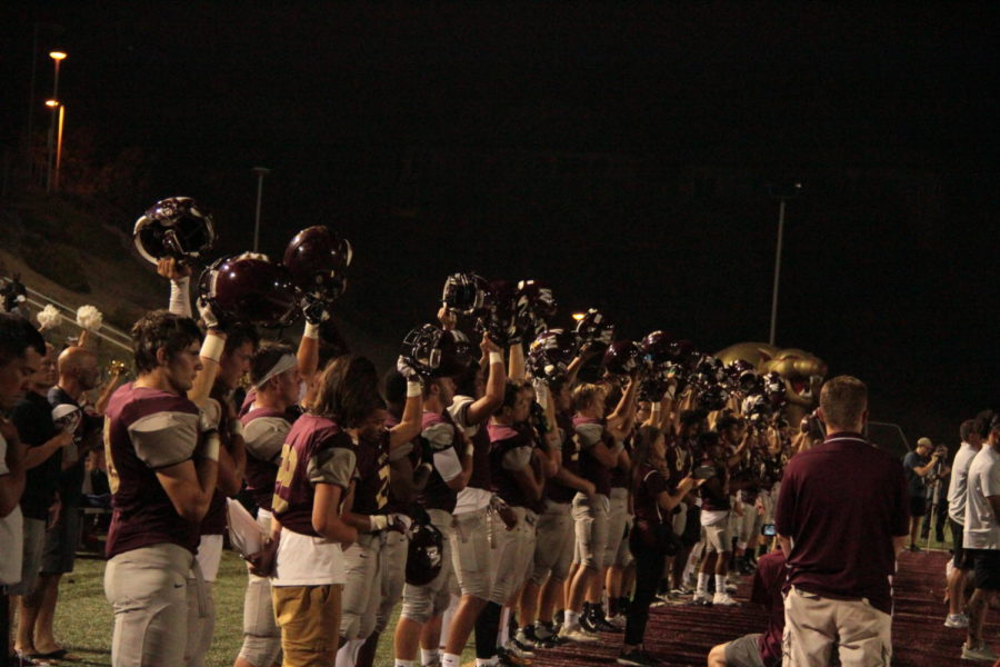 Preparing for the start of the game on Oct. 6, varsity players raise their helmets in honor of the National Anthem. Photo by Blake Wong.