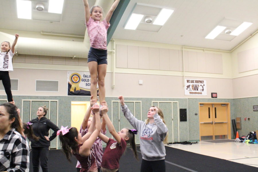 Before running their competition routine full-out, Kylie McLendon helps a stunt group warm up at Whitney Junior Wildcats cheer practice. Photo by Emily Pontes. 
