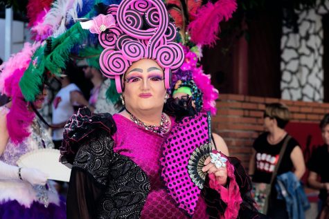 Dressed in a pink drag costume, a performer poses for a photo during a parade. The term “drag” refers to the act of extravagantly dressing and acting as a gender different than one’s own, often in a performance-based environment. Drag may include the impersonation of a famous individual, or dancing or singing as part of an act. Although drag has been linked to Ancient Greece and William Shakepspeare’s work and has been a historic place of community for queer folks, it is currently under surveillance as state lawmakers across the nation continue to push bans and regulations. Photo by Quito Al via Unsplash.