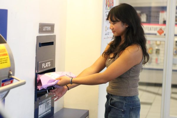 Ara Cobres places her packaged item, a shirt she sold for $12 on Depop, into the flats parcel section at the United States Postal Service (USPS) office May 10. Photo by Riley Rust